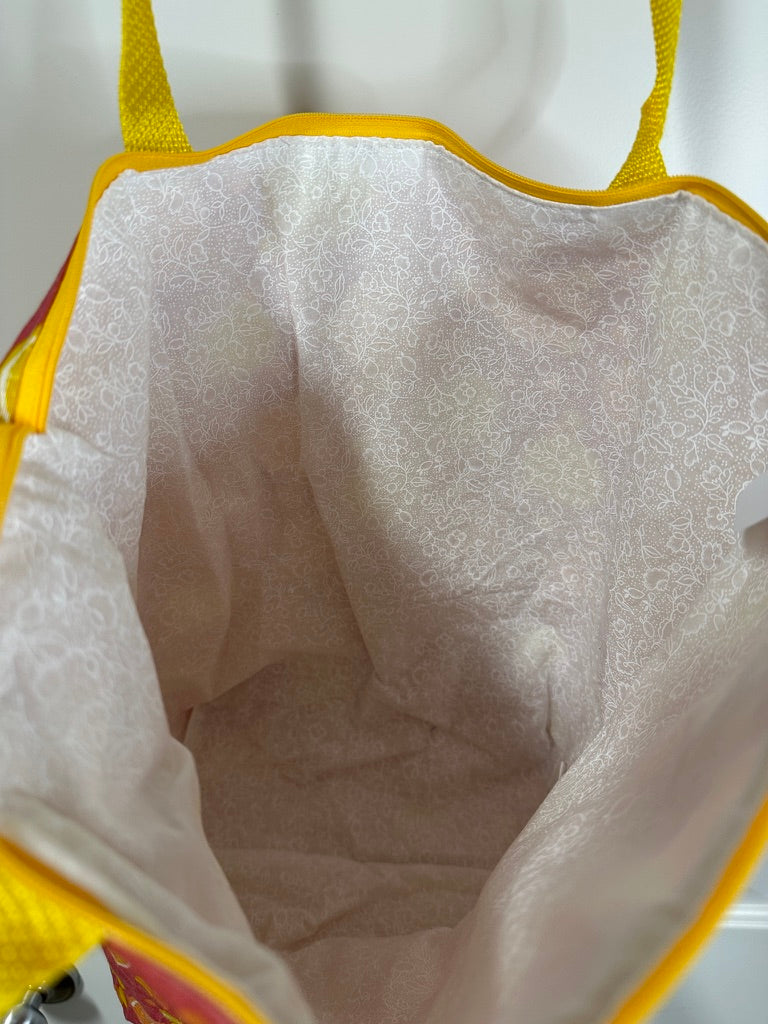 This tote bag has yellow handles and a yellow zipper. The fabric pattern is orange and lemon slices on a pink background, with juice drops and polka dots matching the yellow and orange citrus slices. This photo is showing the white lining.