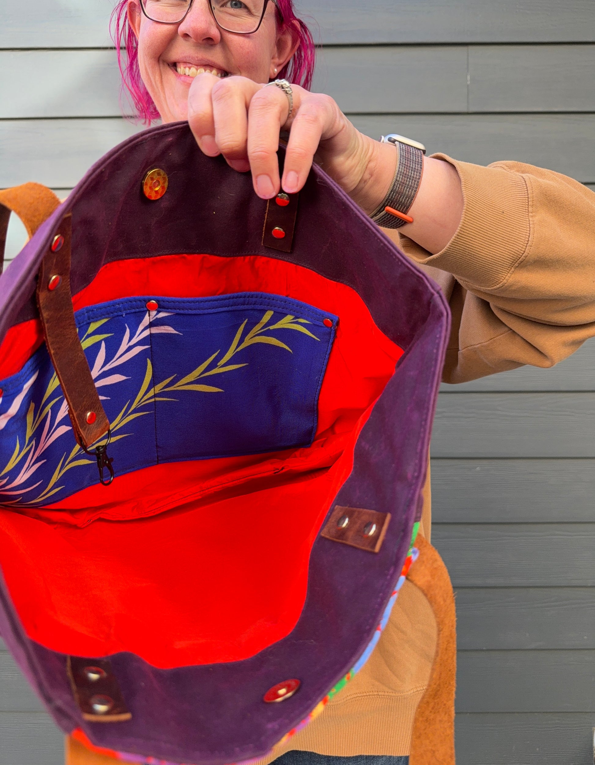 Person holding a colourful bag with floral design against a grey wall. Orange lining with bright blue interior slip pocket