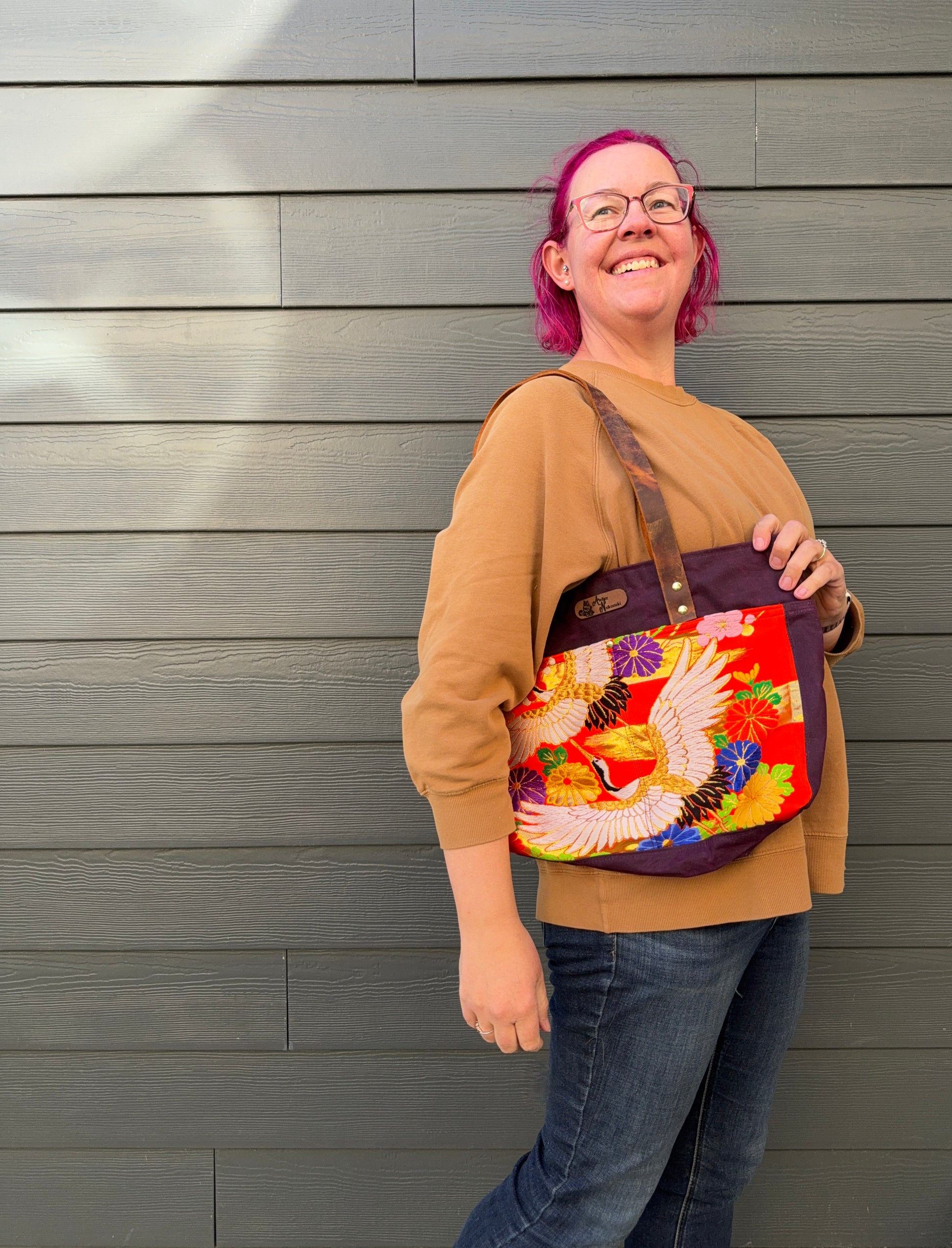 Person holding a colourful bag with cranes and large florals on orange against a grey wall.