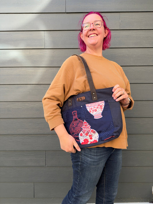 Woman holding a navy tote bag with Japanese vases elements against a gray wall.