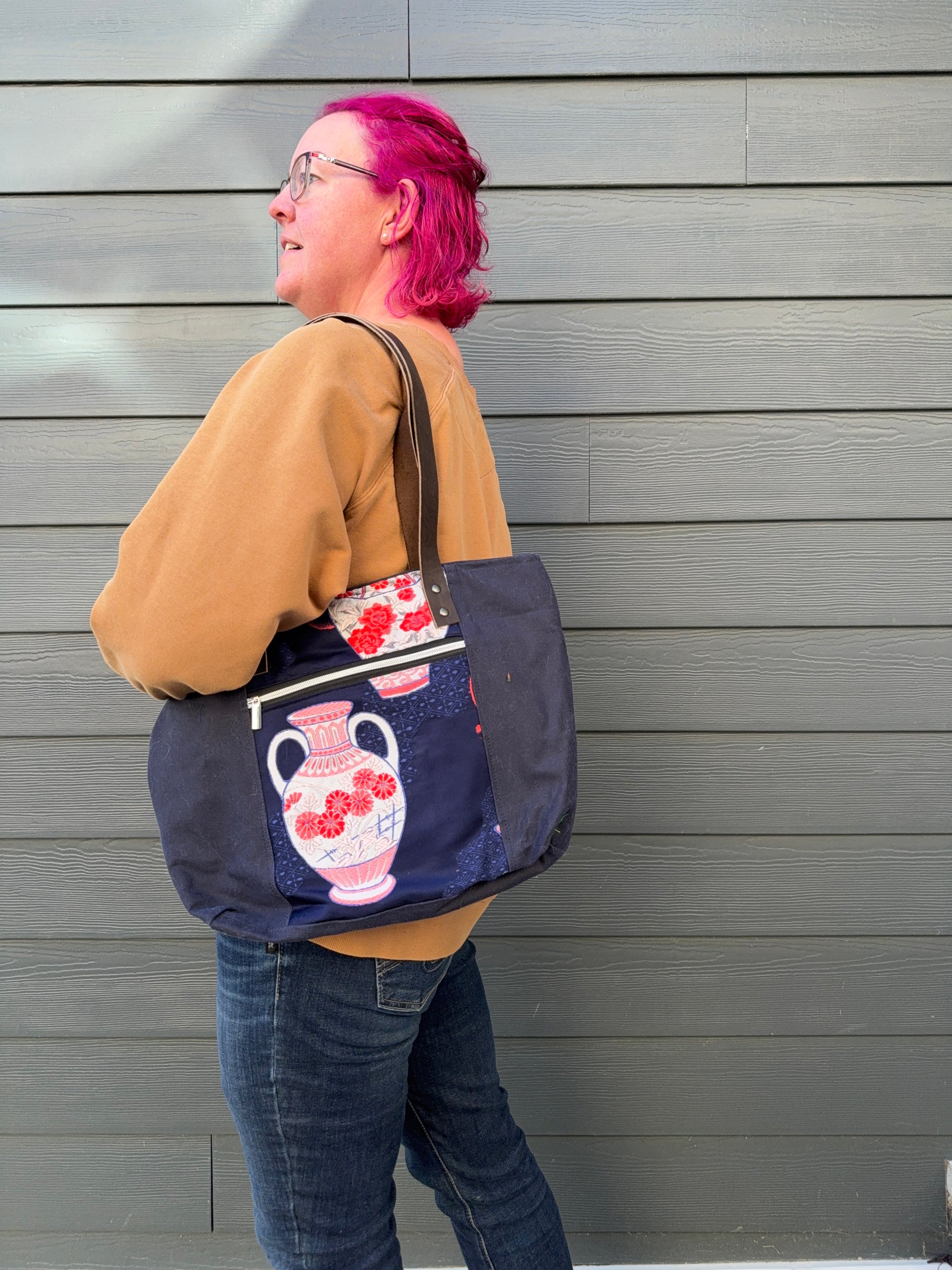 Person with pink hair wearing a navy blue tote bag with a vase design against a grey background