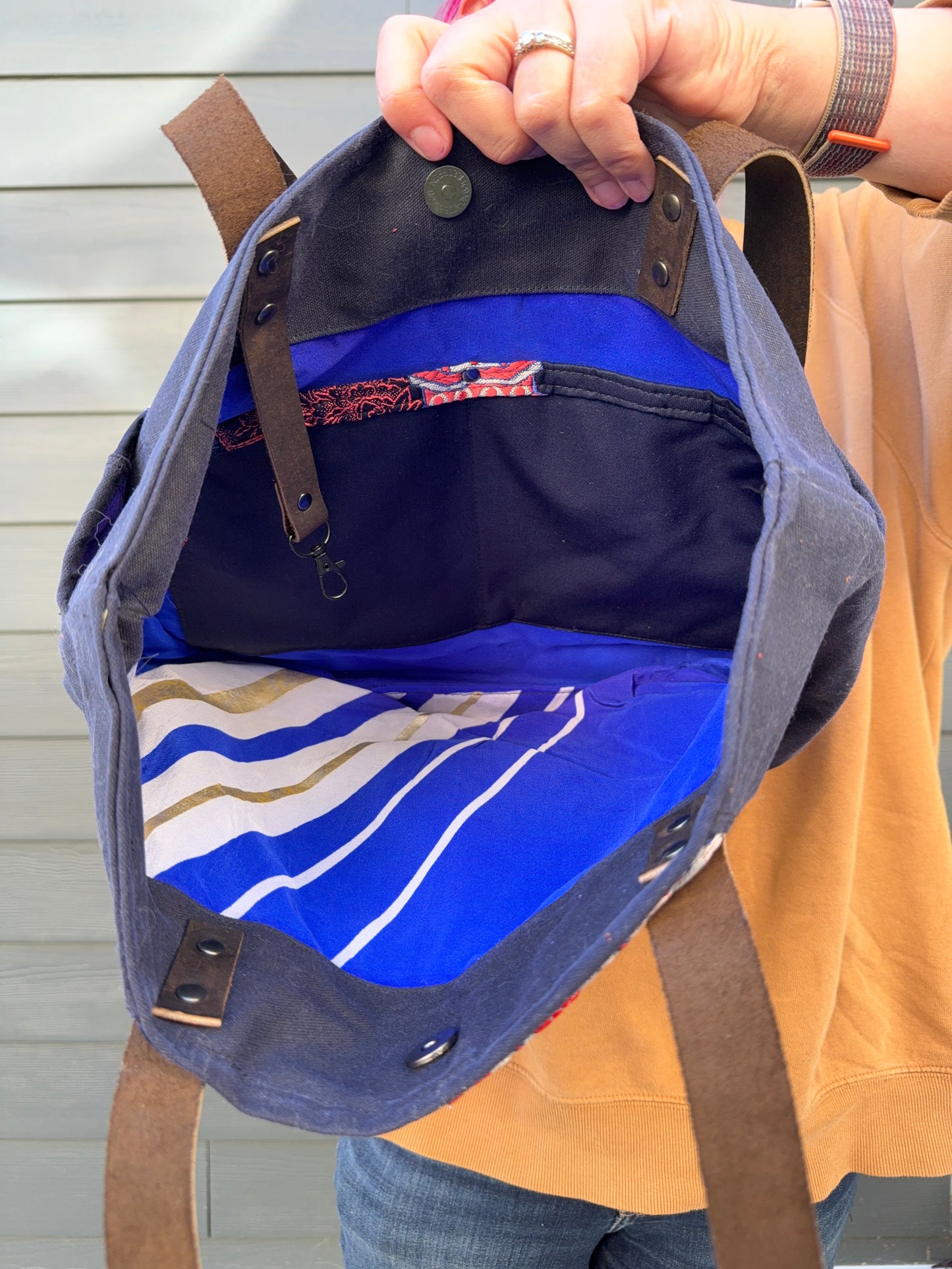 Blue bag with a brown strap held by a person against a grey background