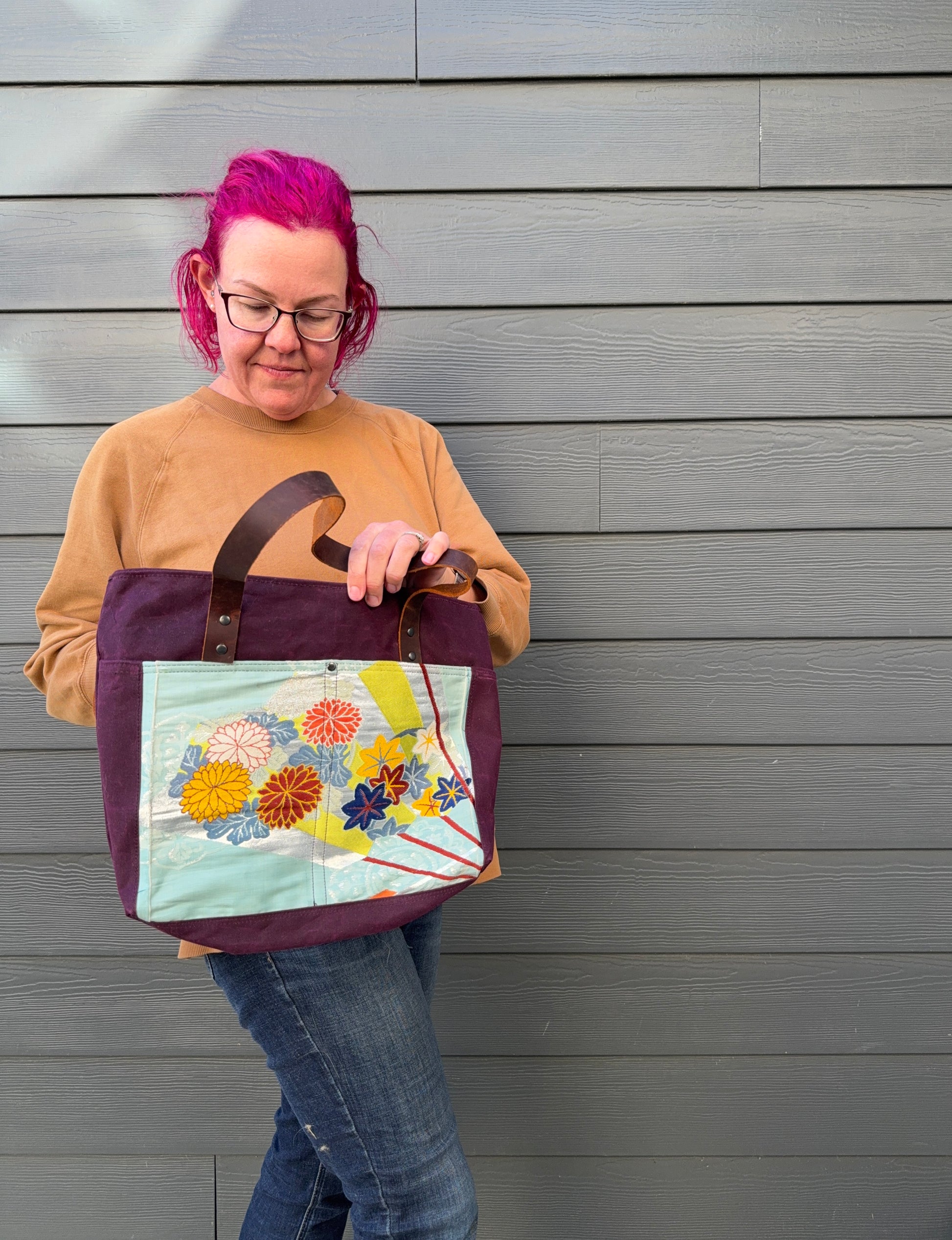 Person holding a tote bag with floral design against a grey wall
