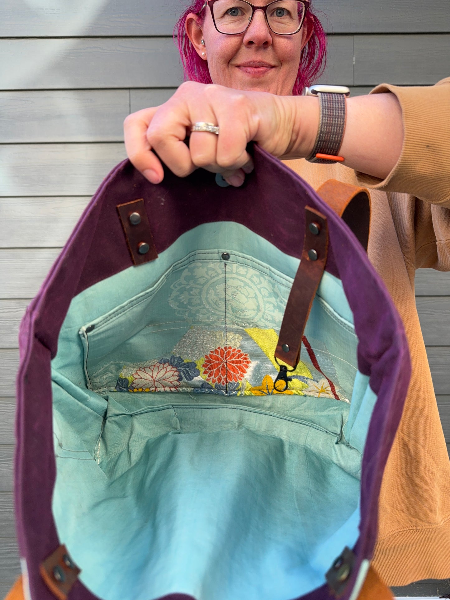 Person holding a purple bag with floral patterned lining. Lining is same aqua and pattern as exterior.