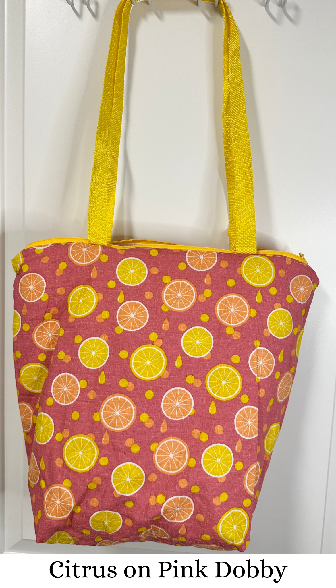 This tote bag has yellow handles and a yellow zipper. The fabric pattern is orange and lemon slices on a pink background, with juice drops and polka dots matching the yellow and orange citrus slices.