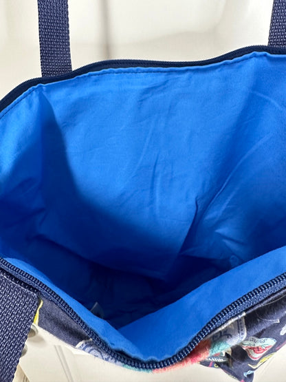 This tote has navy handles and a navy zipper; the print is various retro styled fruit and jam labels on a background of navy; the labels are bright against the background. This photo shows that the lining is a bright sky blue.