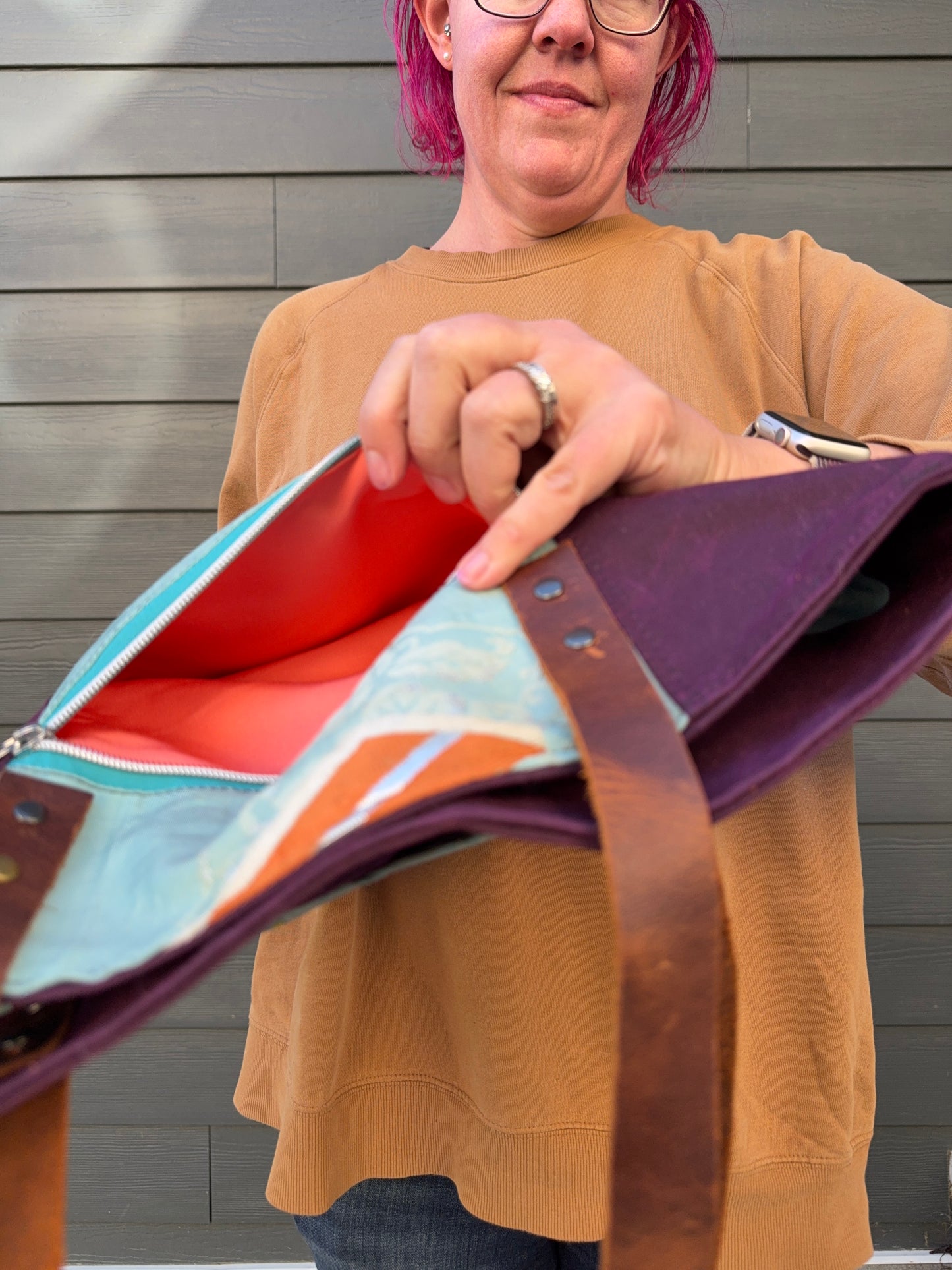 Person holding a colorful handbag against a grey background; showing off exterior zipper pocket lining of coral coloured obi.