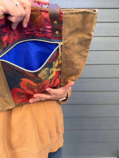 Woman holding a brown waxed canvas bag (framing poppies on navy obi) with colourful interior lining against a grey background.