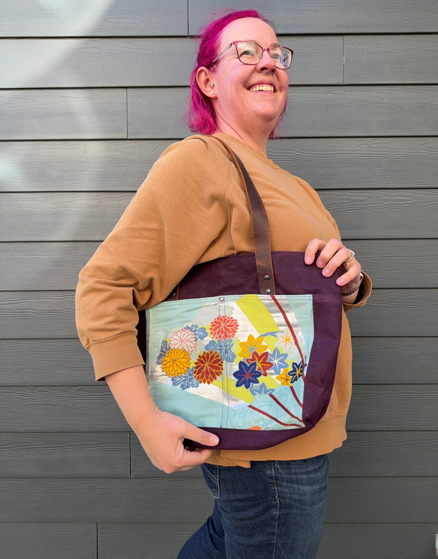 Woman holding a fan patterned with florals against an aqua background. All against a grey background.