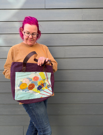 Person holding a tote bag with floral design against a grey wall