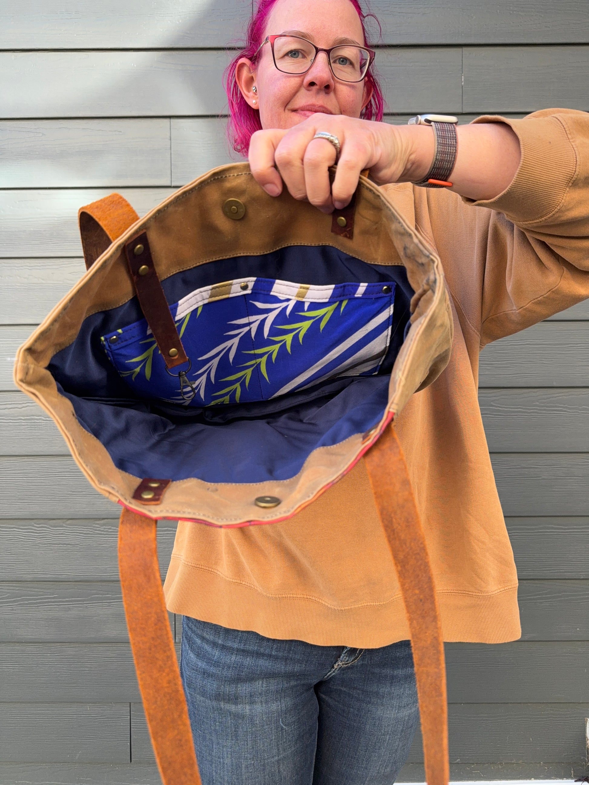 Person holding a tan waxed canvas bag with a blue interior against a grey background